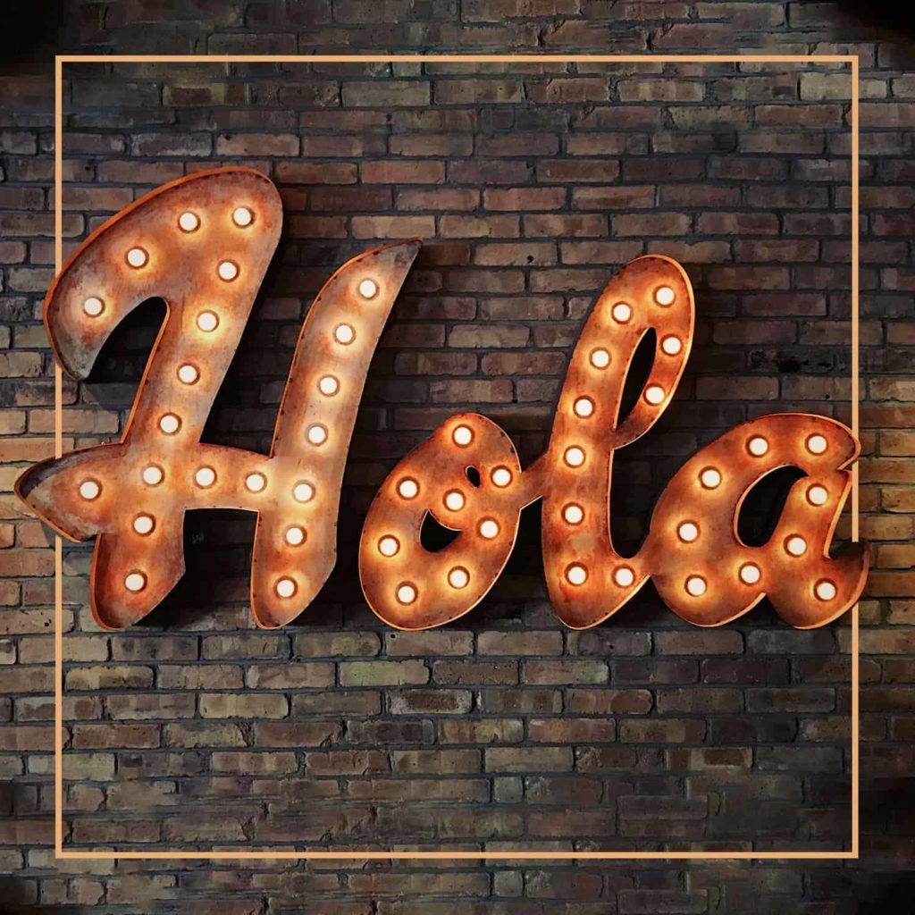 Light up sign on a brick wall saying Hola